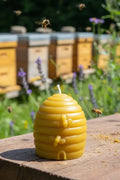 Beeswax candle shaped like a beehive with bees and bee boxes in the background.