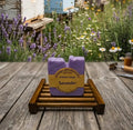 Lavender soap bar on a wooden coaster with a lavender field and beehive in the background