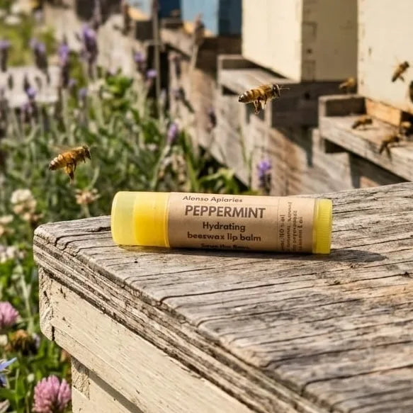 Beeswax lip balm with peppermint flavor on a wooden surface with bees and beekeeping equipment in the background.